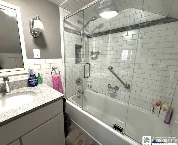 full bath featuring bath / shower combo with glass door, vanity, tile walls, and wood finished floors