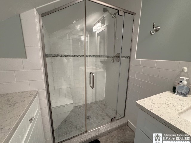 full bath with vanity, a wainscoted wall, a shower stall, and tile walls