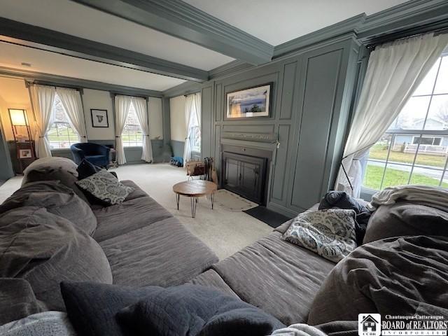 living room featuring a fireplace with flush hearth, beam ceiling, and light colored carpet