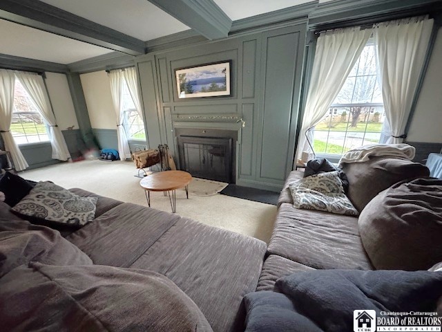 carpeted living room featuring a fireplace with flush hearth, a decorative wall, and beam ceiling