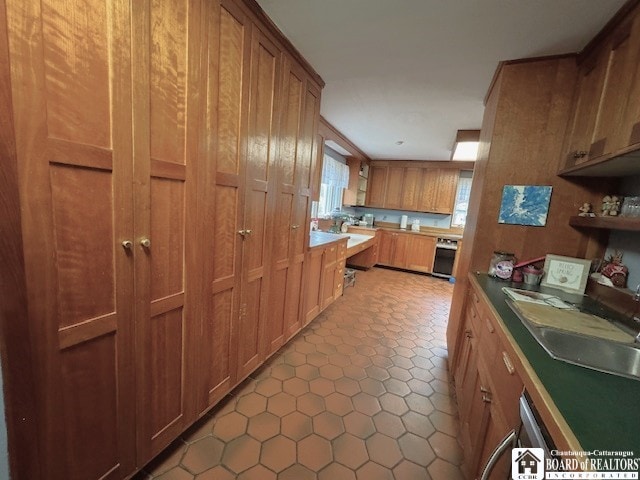 kitchen with light tile patterned flooring, open shelves, brown cabinetry, and a sink