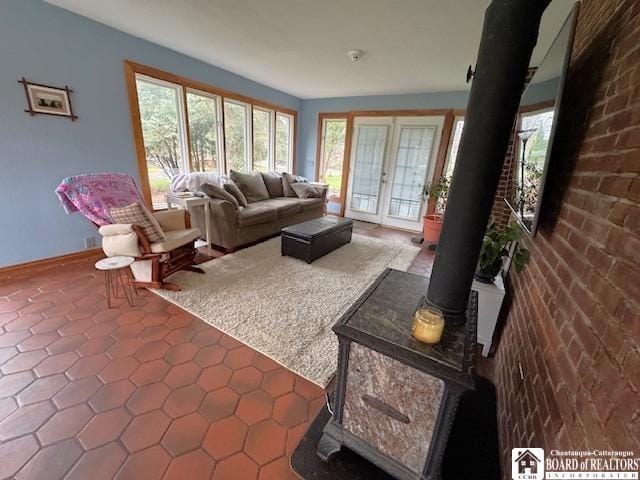 tiled living area featuring baseboards, brick wall, a healthy amount of sunlight, and a wood stove