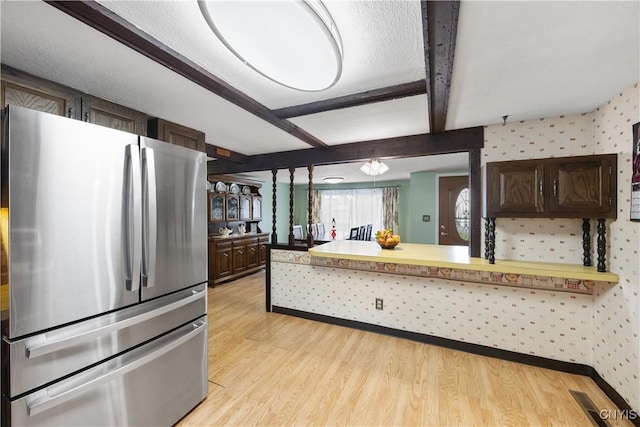 kitchen with dark brown cabinets, freestanding refrigerator, a peninsula, wallpapered walls, and light wood-type flooring