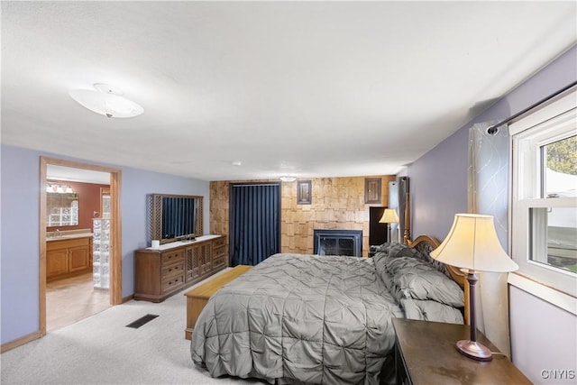 bedroom with connected bathroom, light colored carpet, a large fireplace, baseboards, and visible vents