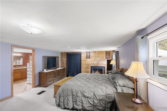 bedroom with light colored carpet, ensuite bath, a glass covered fireplace, baseboards, and visible vents