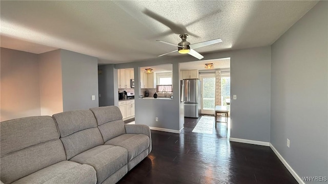 living area with baseboards, ceiling fan, a textured ceiling, and dark wood-type flooring