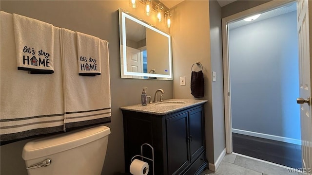 half bathroom featuring vanity, baseboards, tile patterned floors, and toilet