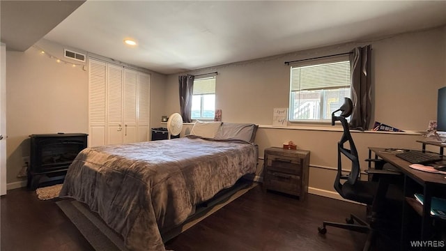 bedroom featuring a wood stove, recessed lighting, baseboards, wood finished floors, and visible vents