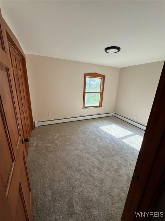 unfurnished bedroom with carpet floors, baseboards, and a baseboard heating unit