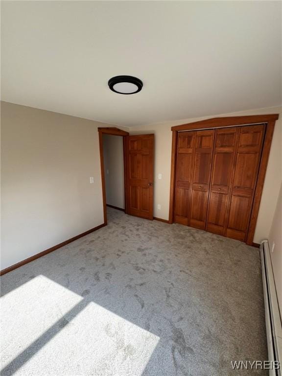 unfurnished bedroom with a closet, baseboards, a baseboard heating unit, and light colored carpet