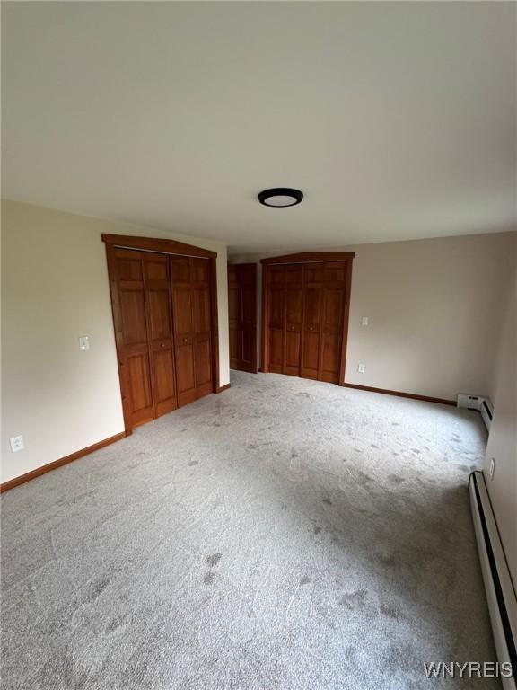 unfurnished bedroom with baseboards, baseboard heating, carpet flooring, and multiple closets