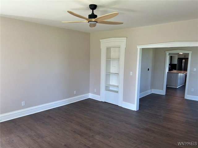 spare room with baseboards, a ceiling fan, dark wood-style flooring, and built in shelves