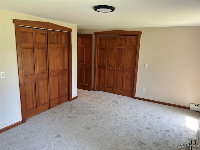 unfurnished bedroom featuring a baseboard radiator, multiple closets, baseboards, and carpet flooring
