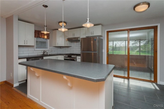 kitchen with under cabinet range hood, dark countertops, appliances with stainless steel finishes, and decorative backsplash