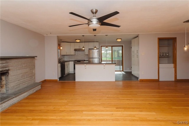 unfurnished living room with a ceiling fan, baseboards, a stone fireplace, and light wood finished floors