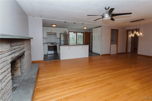 unfurnished living room with baseboards, a ceiling fan, light wood-type flooring, and a stone fireplace