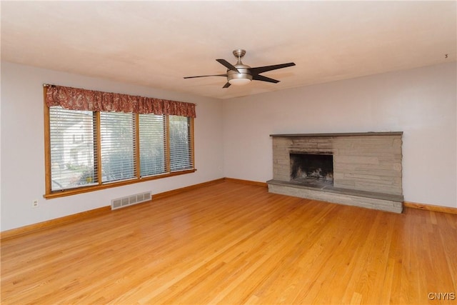 unfurnished living room with light wood-style floors, a fireplace with raised hearth, a ceiling fan, baseboards, and visible vents
