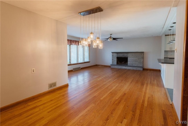 unfurnished living room featuring visible vents, a fireplace with raised hearth, light wood-style floors, and ceiling fan with notable chandelier