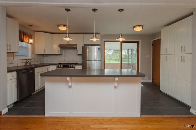 kitchen featuring dark countertops, appliances with stainless steel finishes, a breakfast bar area, decorative backsplash, and under cabinet range hood