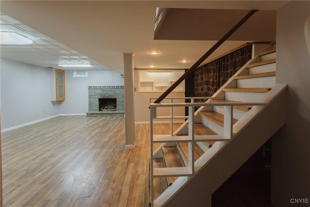 stairway with baseboards, wood finished floors, and a fireplace