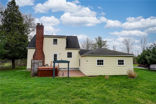 rear view of house with a hot tub, a patio, a yard, and a chimney
