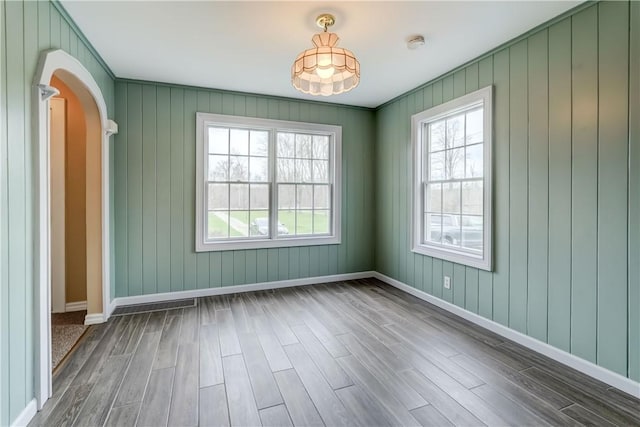 spare room with arched walkways, baseboards, and wood finished floors