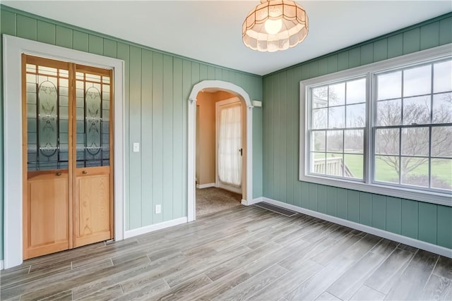 empty room featuring baseboards, arched walkways, and wood finished floors