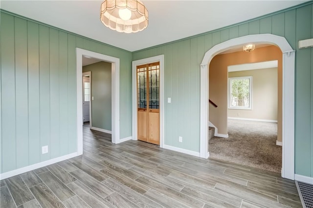 unfurnished room with arched walkways, baseboards, stairs, and wood finished floors