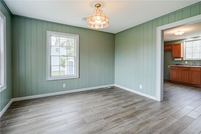 unfurnished dining area featuring baseboards, a sink, and light wood finished floors