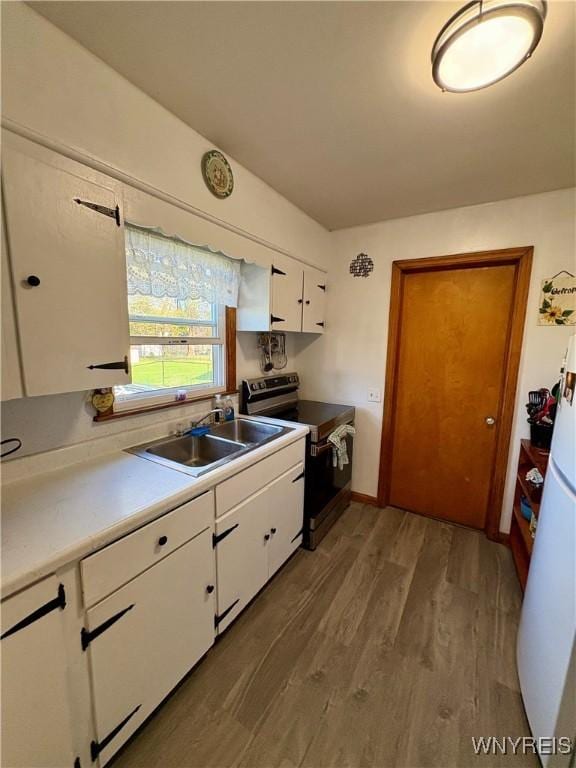 kitchen with a sink, wood finished floors, light countertops, white cabinets, and electric stove