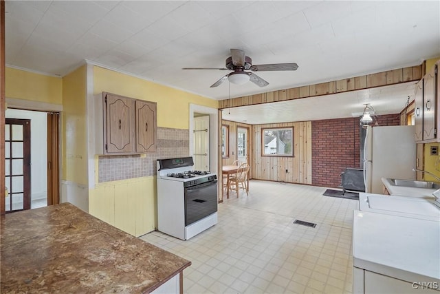 kitchen with ceiling fan, visible vents, wood walls, a sink, and white appliances