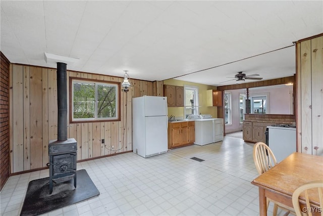 kitchen featuring wooden walls, a wood stove, white appliances, washer / clothes dryer, and a healthy amount of sunlight