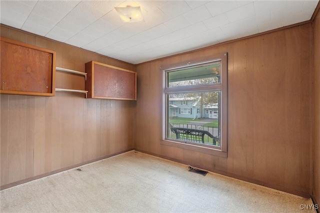 unfurnished room featuring wooden walls, visible vents, and light carpet