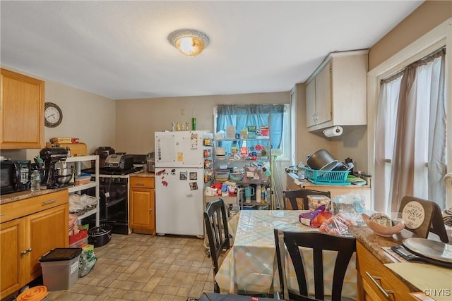 kitchen with freestanding refrigerator, stone finish flooring, a healthy amount of sunlight, and black microwave