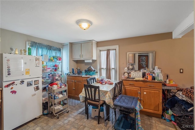 kitchen featuring plenty of natural light, freestanding refrigerator, brown cabinetry, and stone finish floor