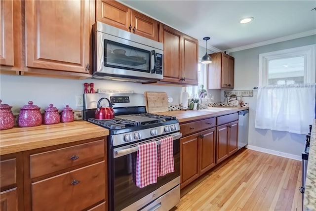 kitchen with butcher block countertops, crown molding, appliances with stainless steel finishes, a sink, and light wood-style flooring