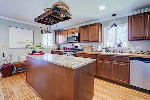kitchen with crown molding, appliances with stainless steel finishes, a sink, and a center island