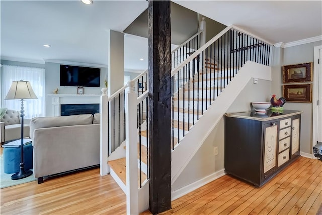 staircase featuring baseboards, ornamental molding, a fireplace, and hardwood / wood-style flooring