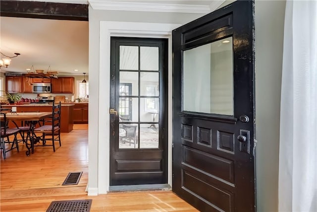 doorway to outside featuring ornamental molding, light wood finished floors, and visible vents