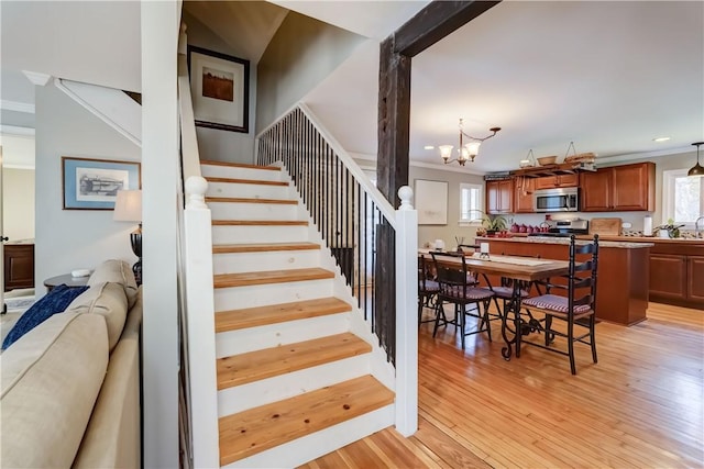 stairway featuring wood-type flooring, an inviting chandelier, and ornamental molding