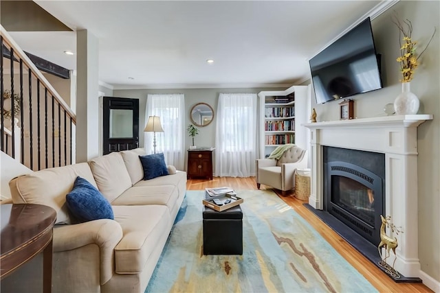 living area with crown molding, a glass covered fireplace, wood finished floors, and stairway