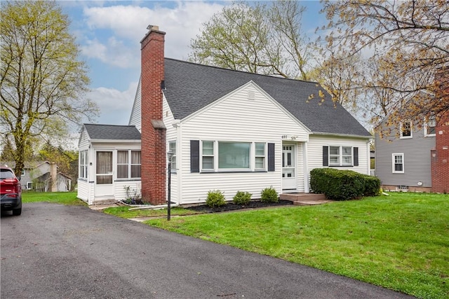 cape cod-style house featuring roof with shingles, a chimney, a sunroom, and a front yard