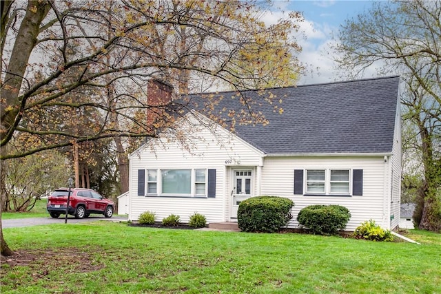 view of front of house featuring a shingled roof, a chimney, driveway, and a front yard