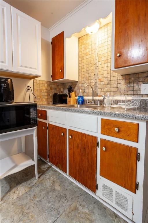 kitchen with a sink, decorative backsplash, white cabinets, and black microwave
