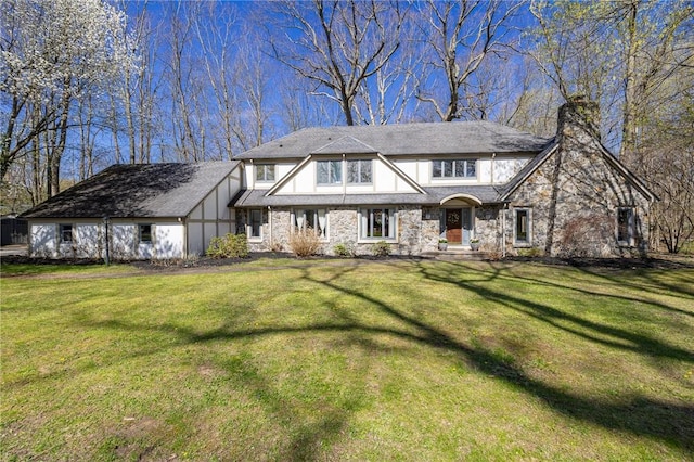 english style home featuring a chimney, stone siding, and a front yard