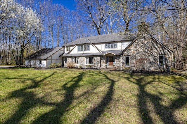 tudor-style house featuring a chimney, a front lawn, and stone siding