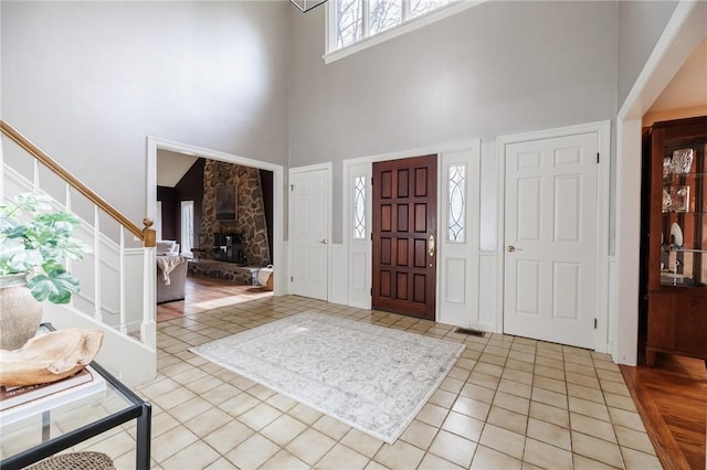 entrance foyer with stairway, a stone fireplace, light tile patterned flooring, and a towering ceiling