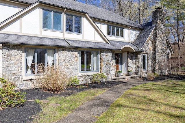 tudor house featuring a chimney, a front lawn, stucco siding, and stone siding