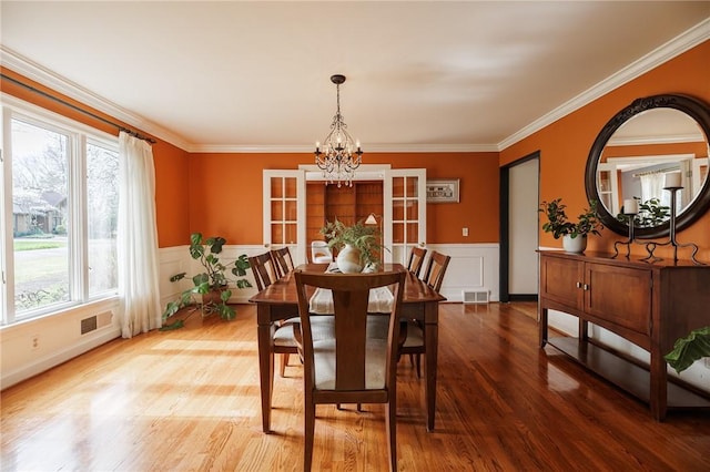 dining area featuring an inviting chandelier, crown molding, wainscoting, visible vents, and wood finished floors