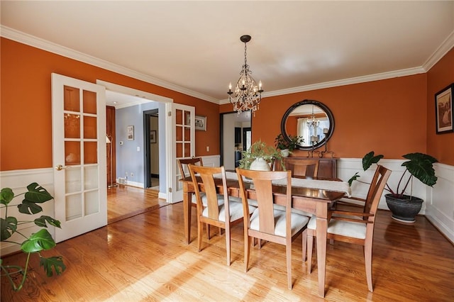 dining space featuring ornamental molding, light wood-style flooring, a wainscoted wall, and a notable chandelier
